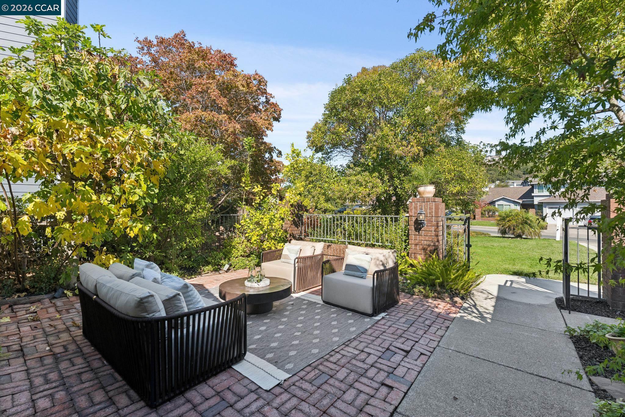Brick patio with cushioned seating, a round table, and leafy garden surroundings.