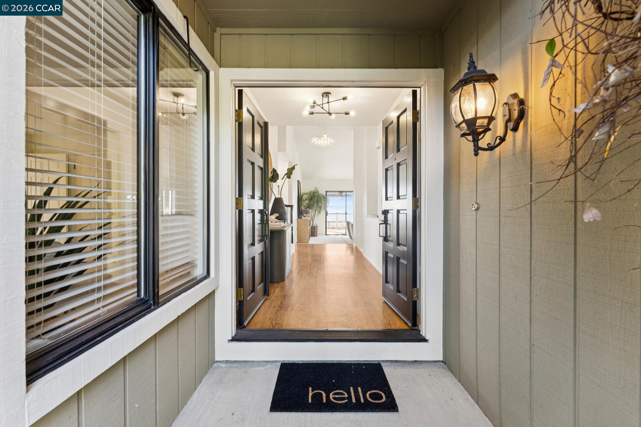Front entry with open black double doors, a wood-floored foyer, and water visible beyond.