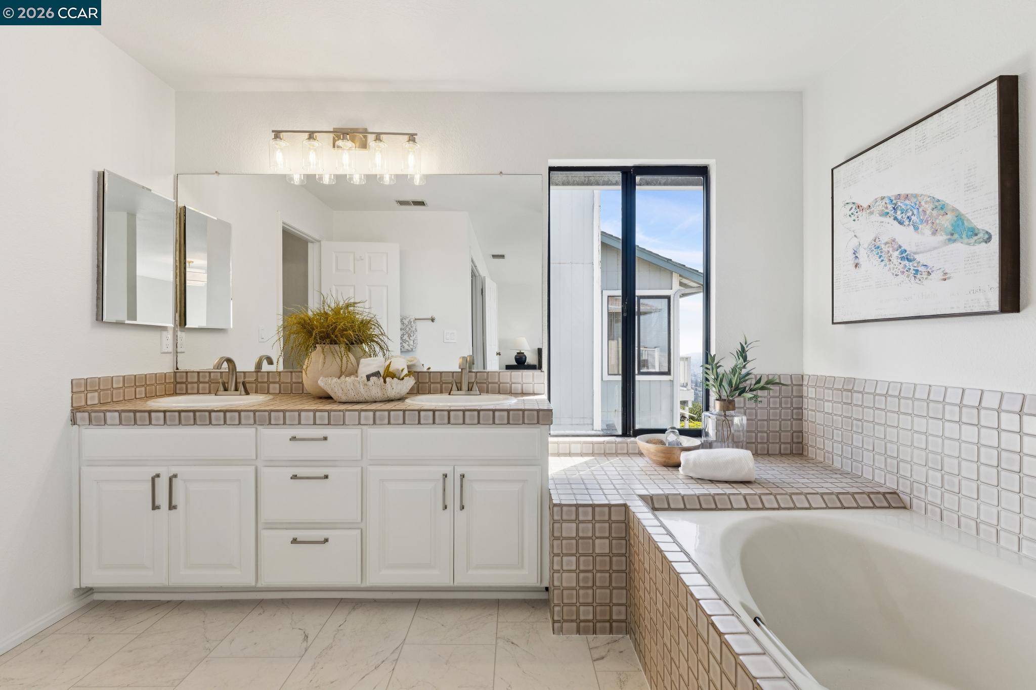 Bright bathroom with double vanity, tiled soaking tub, and a tall window.