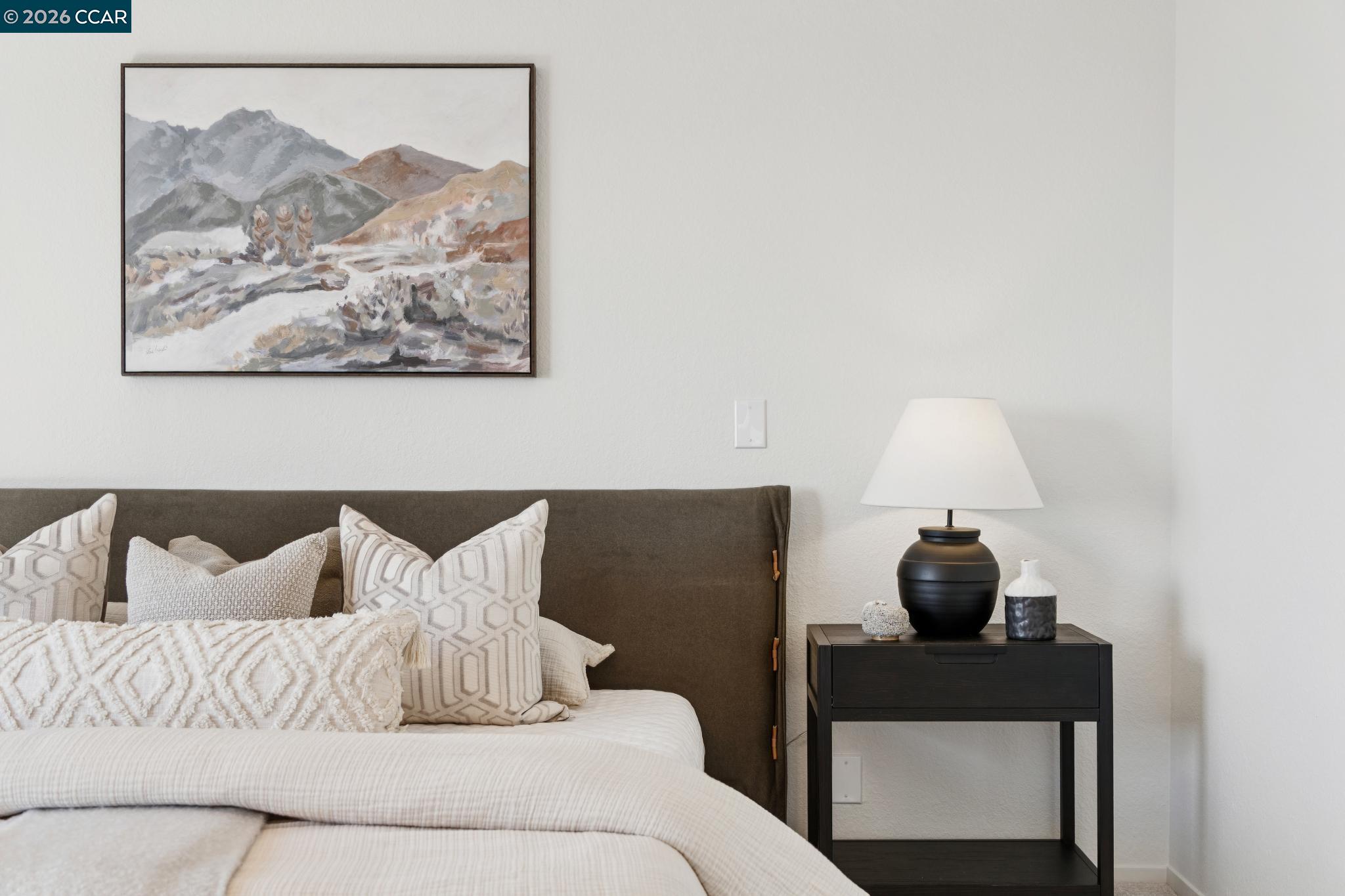 Furnished bedroom with layered white bedding, a dark headboard, and framed mountain landscape.