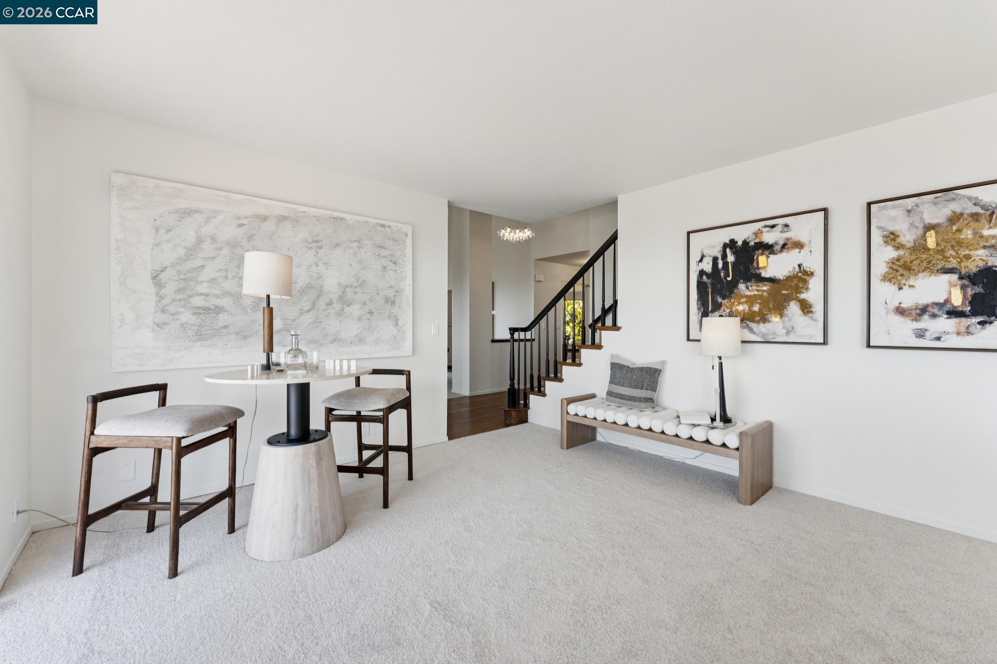 Staged living room with a round table, abstract art, and a staircase with dark railing.