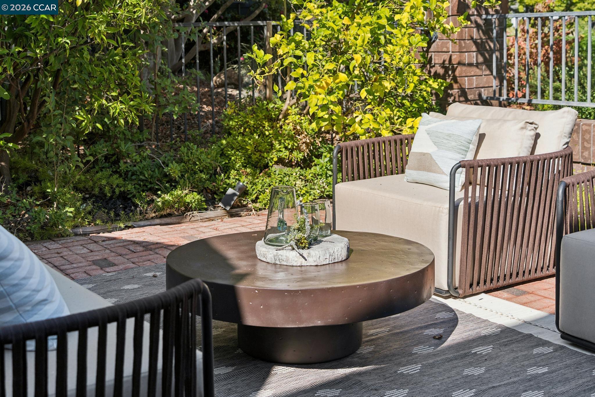 Outdoor patio with cushioned lounge chairs, a round coffee table, and lush garden landscaping.
