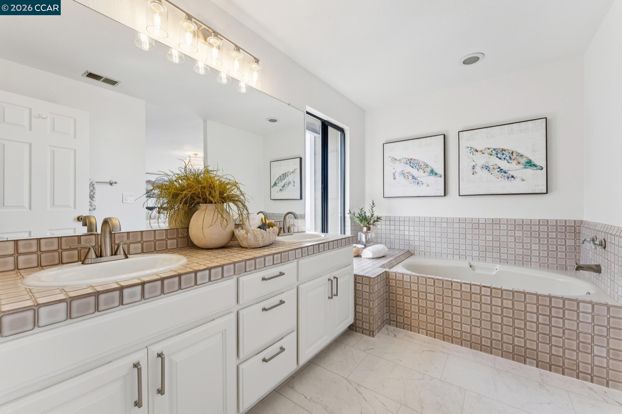Bathroom with a tiled vanity and built-in tub beneath framed sea turtle artwork.