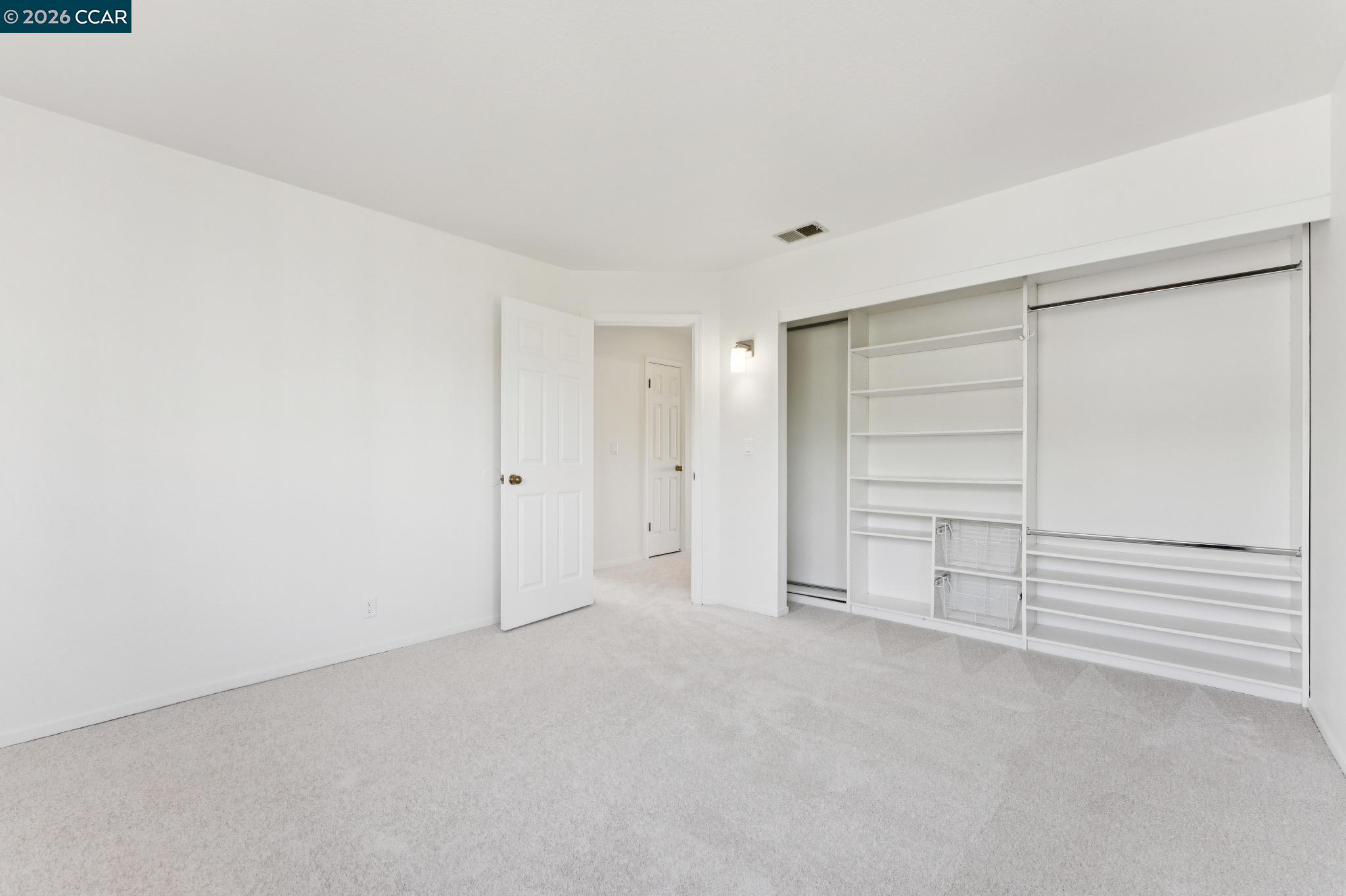 Empty carpeted room with built-in closet organizers and an open doorway.