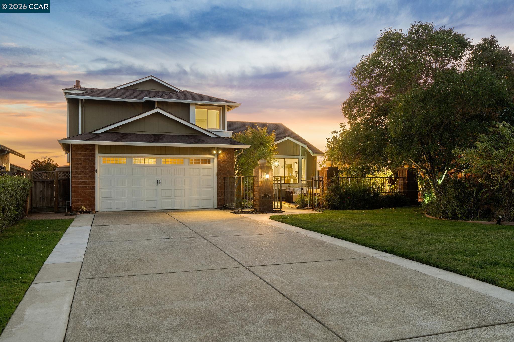 Two-story house with a wide driveway, two-car garage, and illuminated gated entry at dusk.