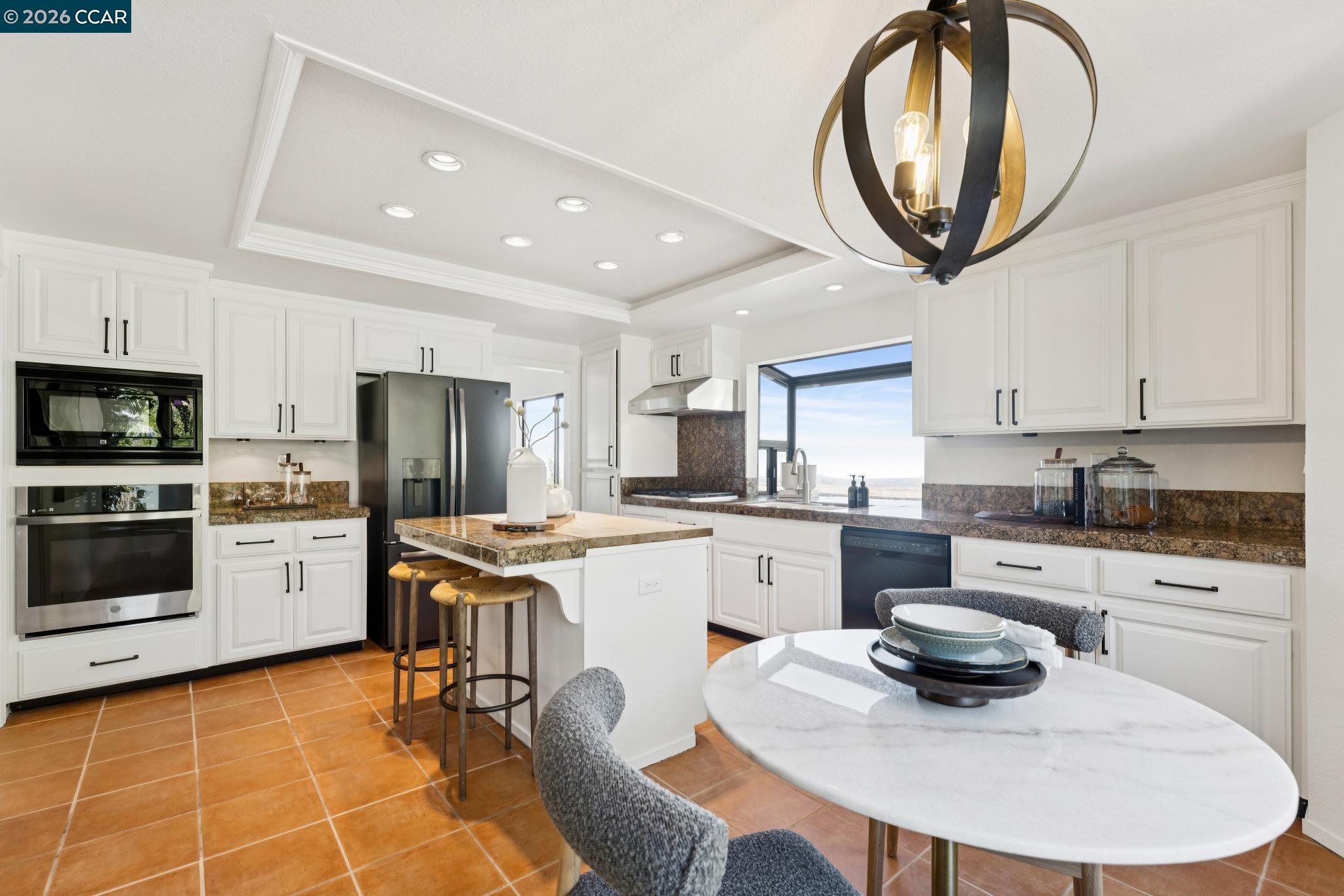 Bright kitchen with white cabinets, granite island, terracotta tile, and a round dining table.