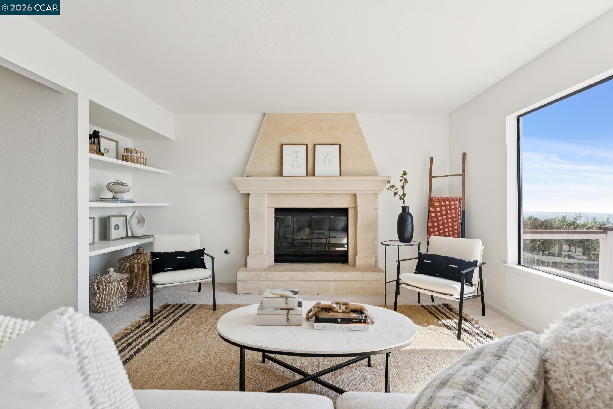Staged living room with a stone fireplace, built-in shelves, and a large window.