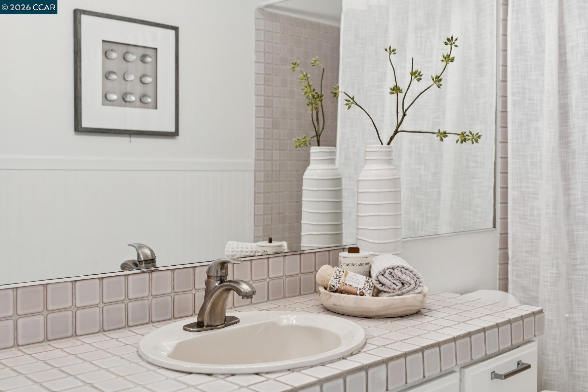 Bathroom vanity with pale pink tile, an oval sink, brushed metal faucet, and decorative vases.