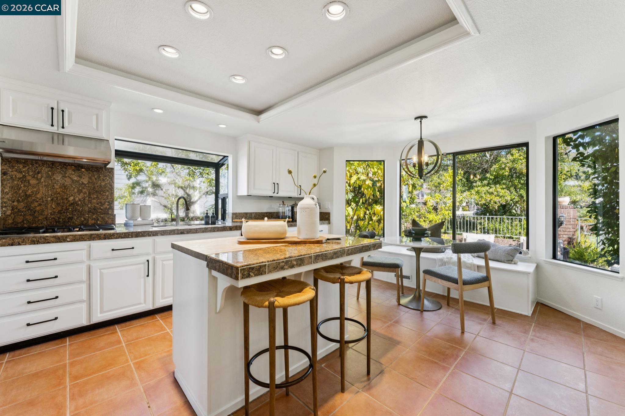 Kitchen with white cabinetry, stone counters, a central island, and large windows overlooking greenery.