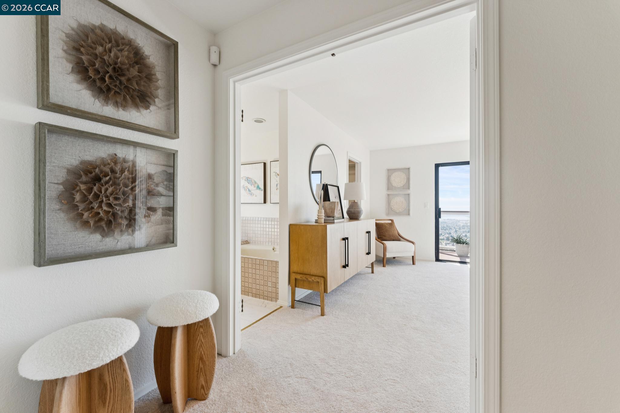 Carpeted foyer with sculptural stools looking into a furnished room and toward a glass balcony door.