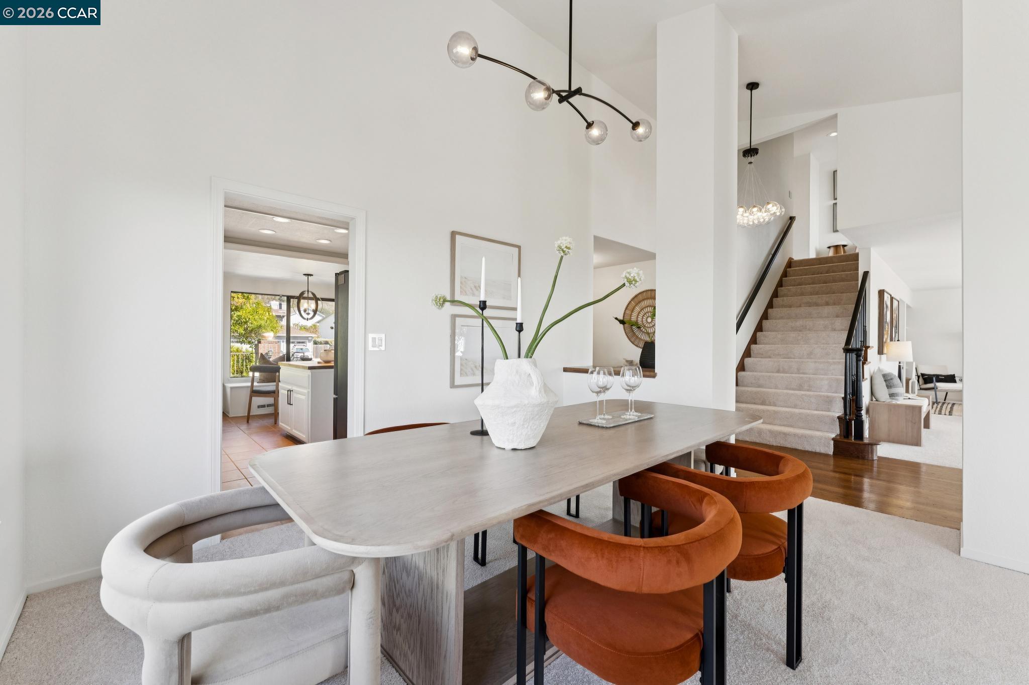 Dining room with a long table, sculptural chairs, modern chandelier, and staircase.