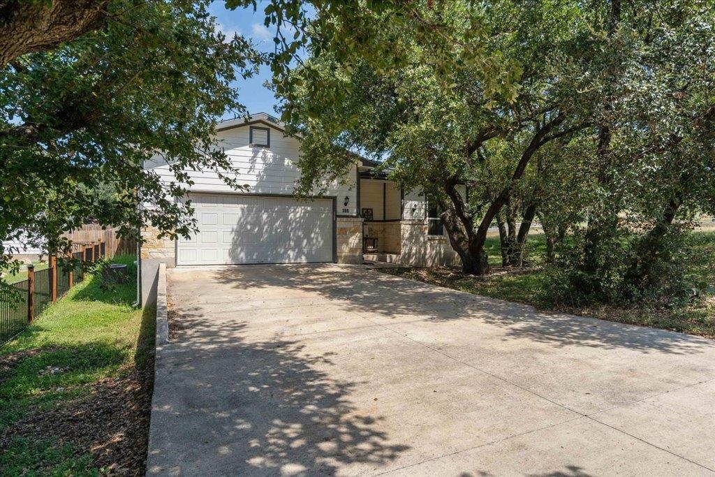 Two-story house with a wide garage and shaded concrete driveway beneath mature trees.