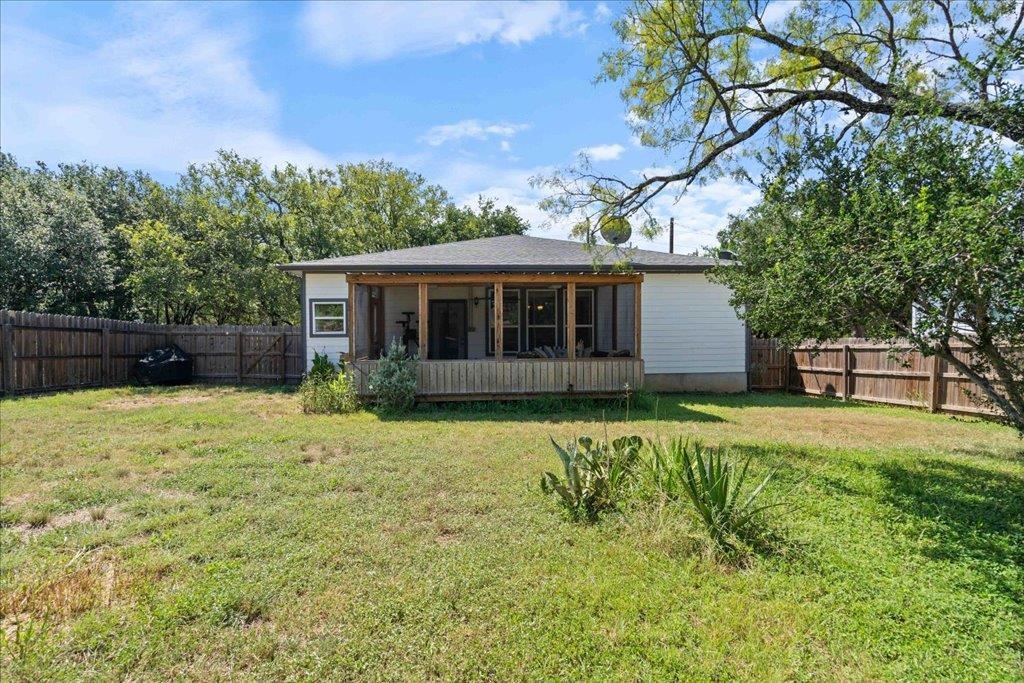 Single-story home with a covered porch behind a broad grassy, fenced yard.