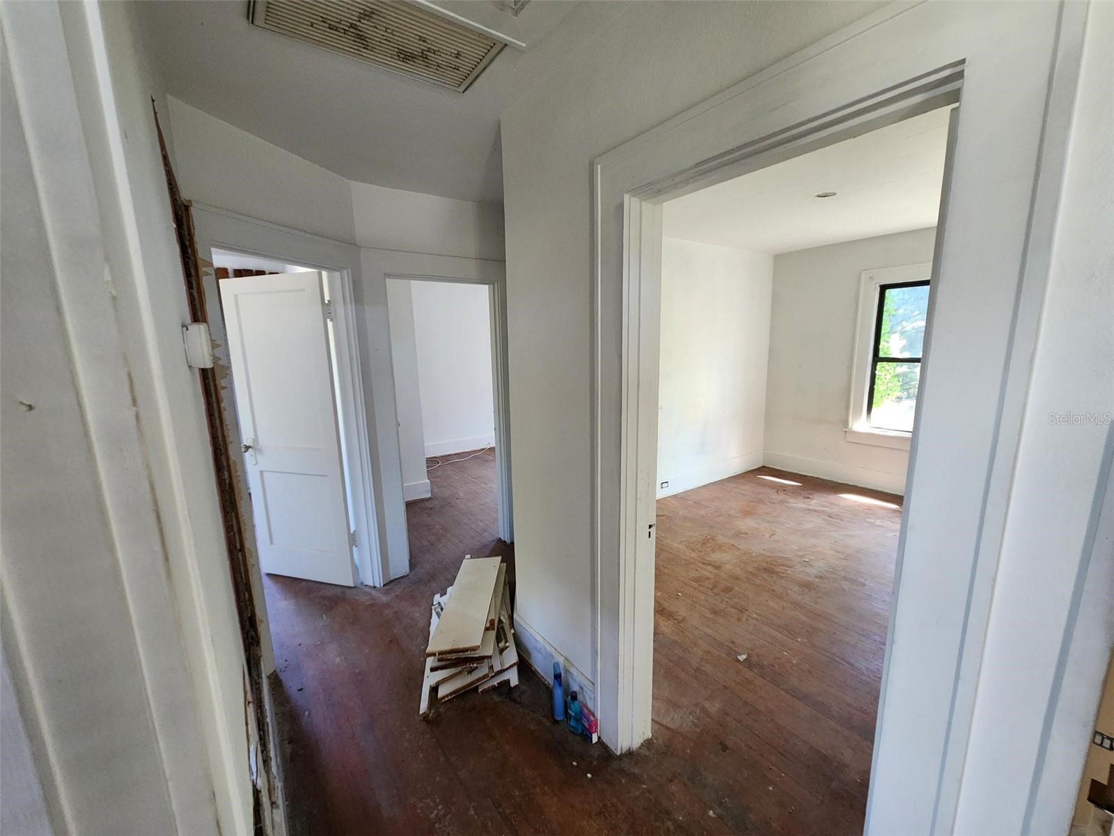 Interior hallway opening into two empty rooms with worn hardwood floors and exposed trim.