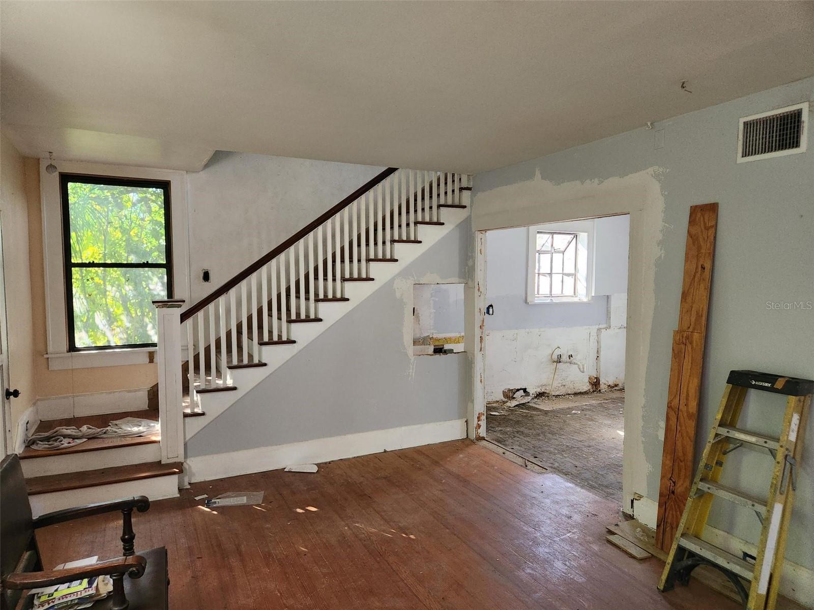 Partially renovated interior with a white staircase, dark wood handrail, and unfinished adjoining room.