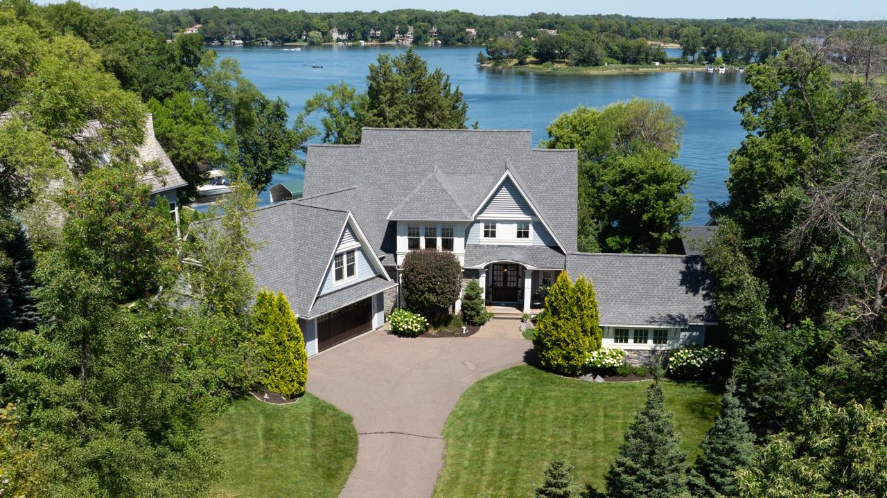 Aerial view of a gray lakeside home, landscaped grounds, and blue water beyond.
