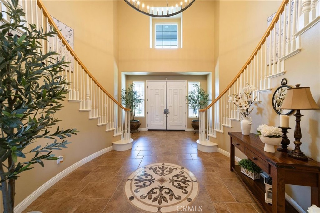 Two-story foyer with twin staircases, white double doors, tiled floor, and a round patterned rug.