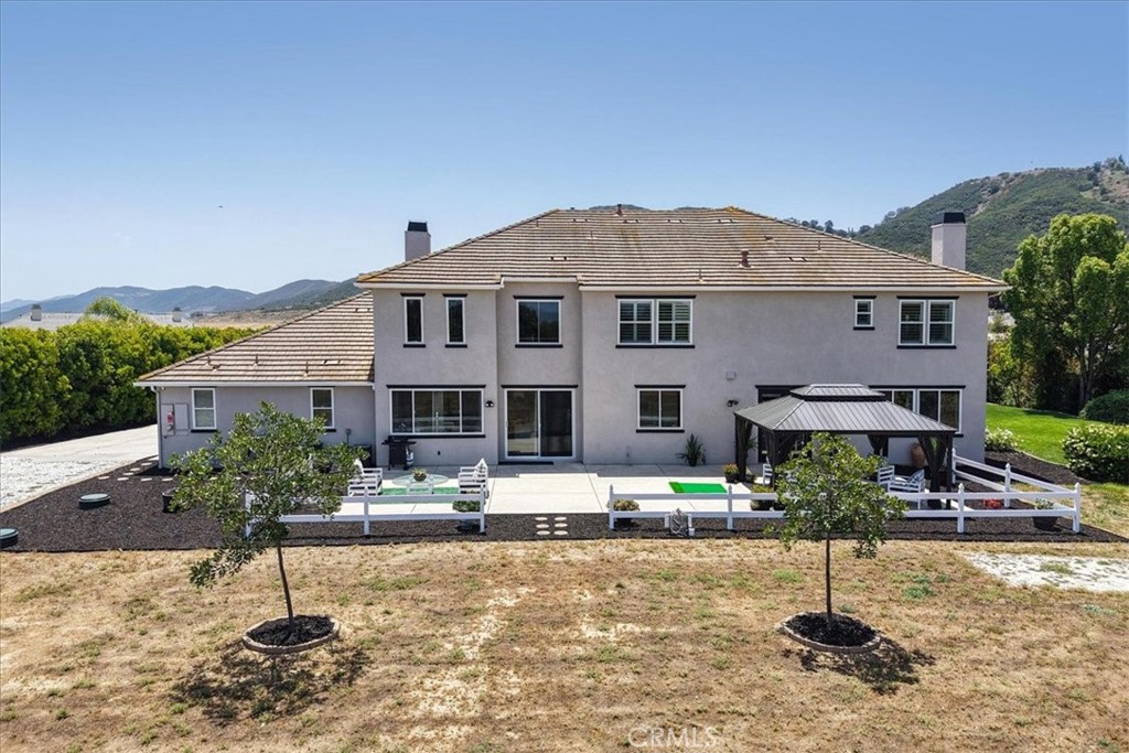 Two-story home viewed from the backyard, with a gazebo, white fence, and hills beyond.