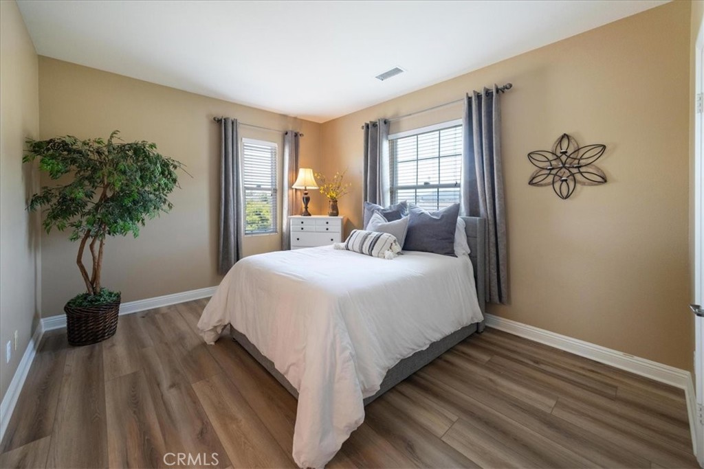 Staged bedroom with a white bed, gray curtains, and wood-look flooring.