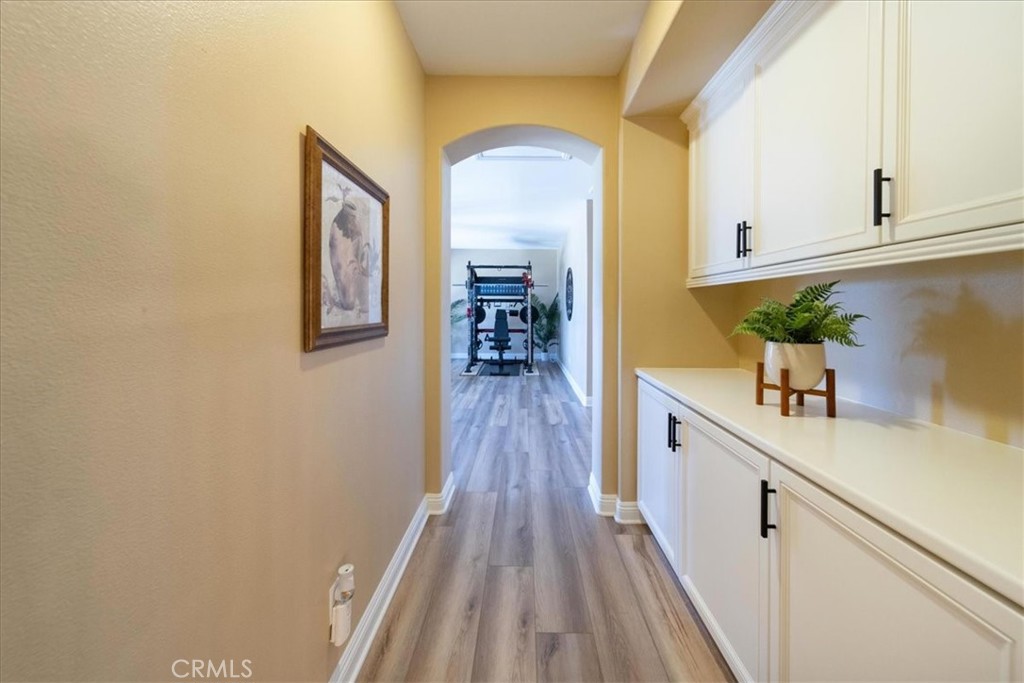 Hallway with white built-in cabinets and wood-look floors leading to a home gym.