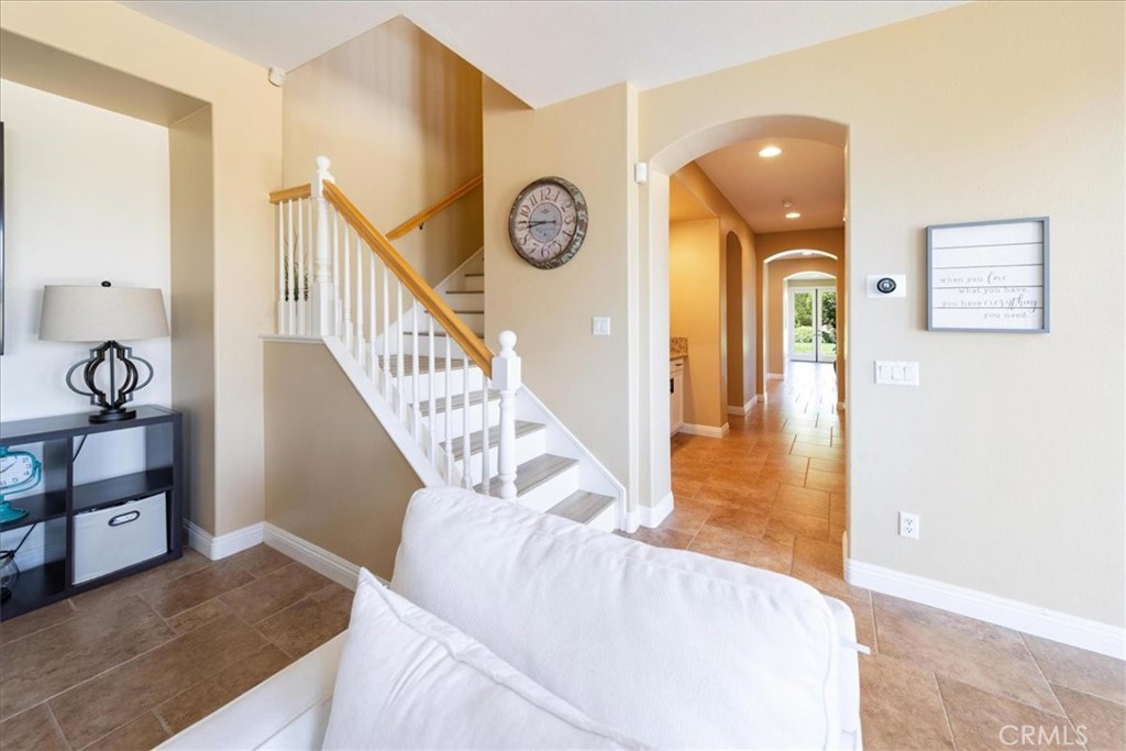 Entryway with a tiled floor, white staircase, wood handrail, and arched hallway.