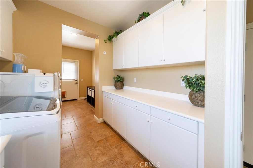 Laundry room with white washer and dryer, built-in cabinets, and tan tile flooring.