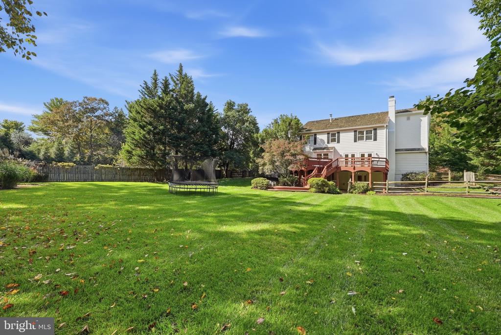White two-story house with a raised deck behind a broad lawn and trampoline.