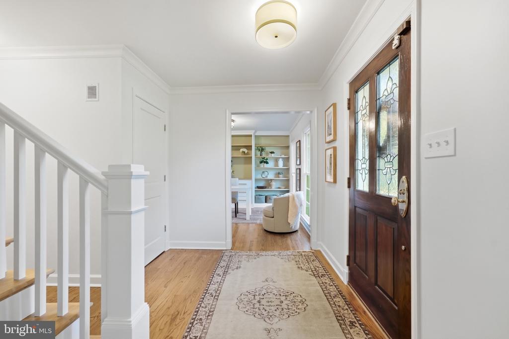 Entry foyer with hardwood floors, a patterned runner, and a dark wood front door with decorative glass.