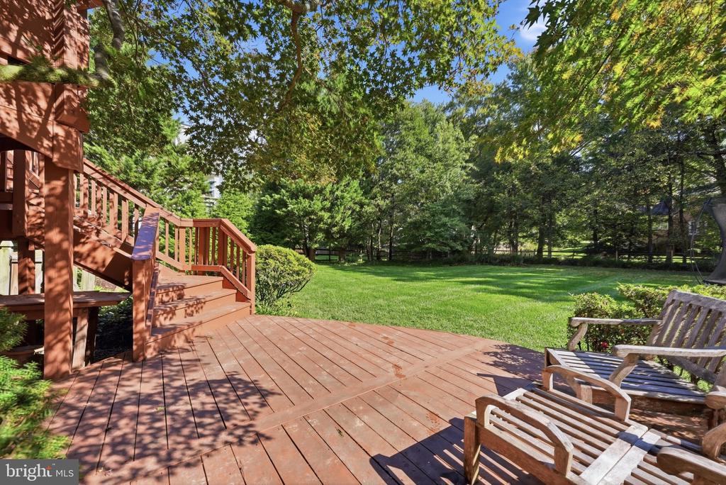 Wooden backyard deck with stairs and patio chairs overlooking a tree-lined lawn.