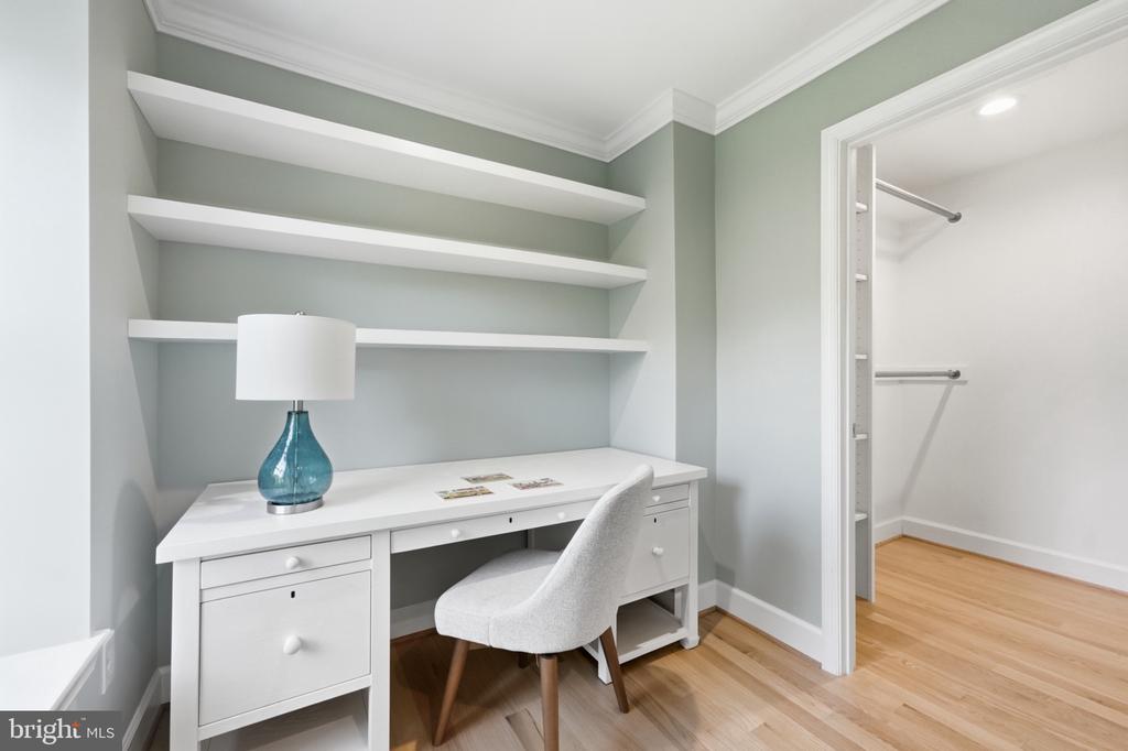 Home office nook with built-in shelves, a white desk, and an upholstered chair beside an open closet.