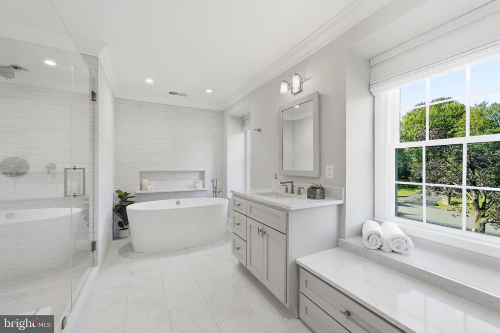 Bathroom with a freestanding soaking tub, glass shower, white vanity, and window seat.