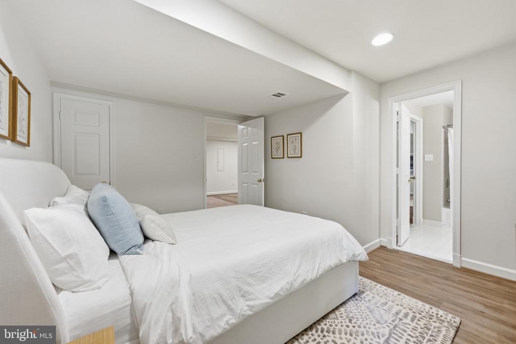 Staged bedroom with a white bed, pale blue accent pillow, patterned rug, and two open doorways.
