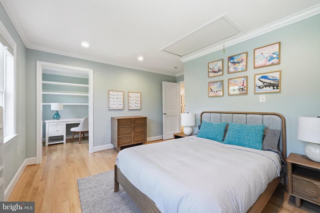 Bedroom with turquoise pillows and airplane artwork, opening to a desk nook with built-in shelves.