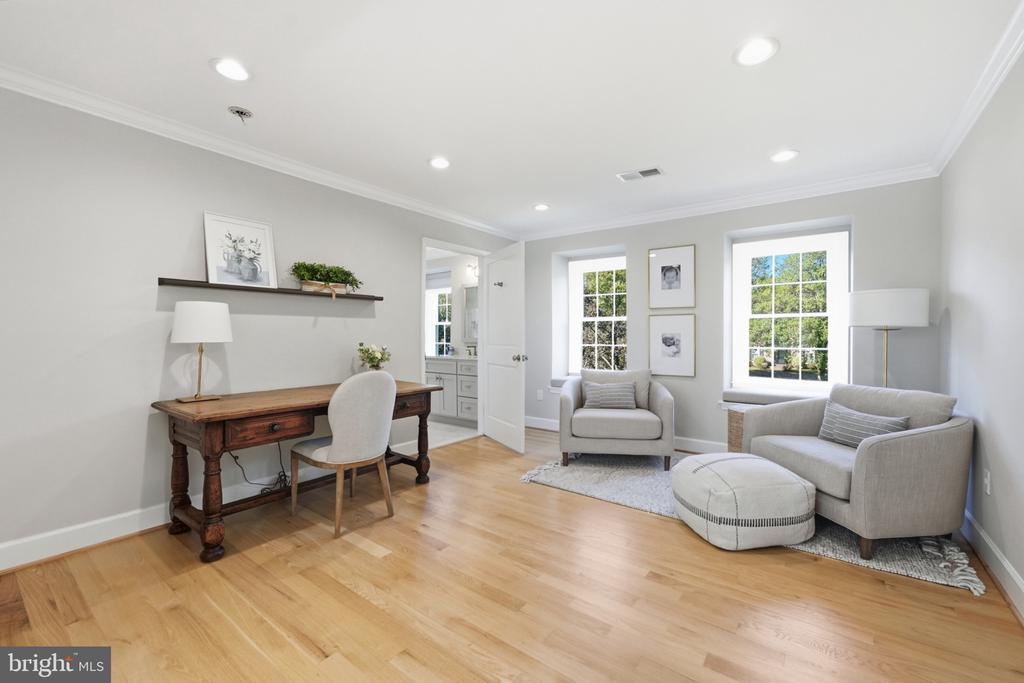 Sitting room with a wooden desk, two armchairs, and large windows.