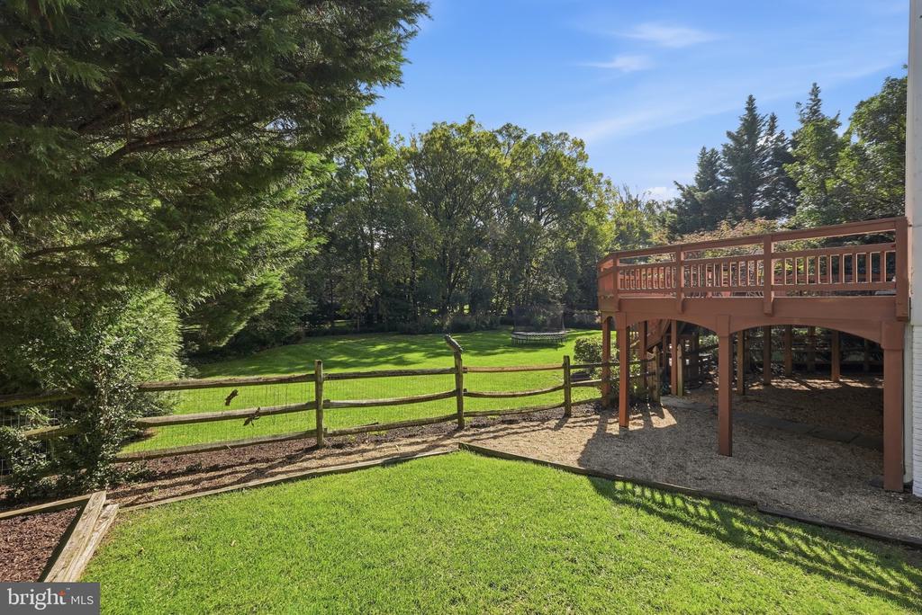 Backyard lawn bordered by mature trees and a split-rail fence, with an elevated wooden deck.