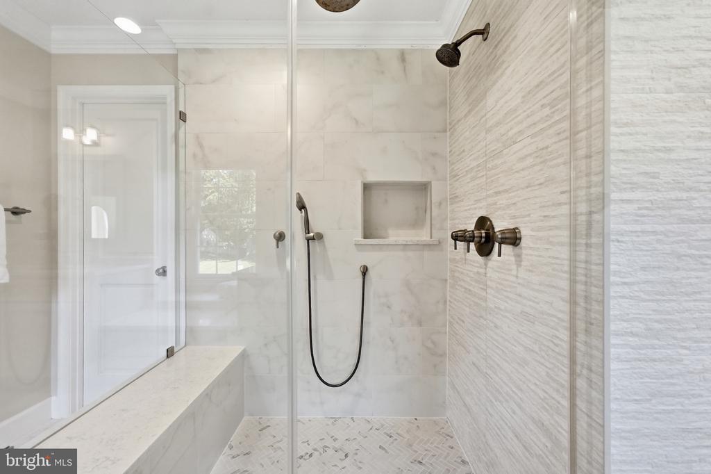Walk-in shower with white marble-look tile, a built-in bench, and bronze fixtures.