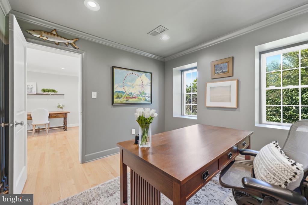 Home office with a large wooden desk, gray walls, and windows overlooking greenery.