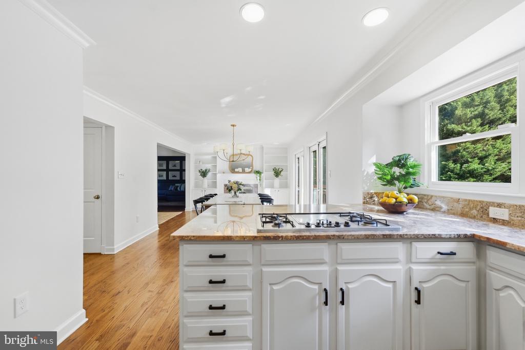 Bright white kitchen with granite counters, a gas cooktop, and hardwood floors.