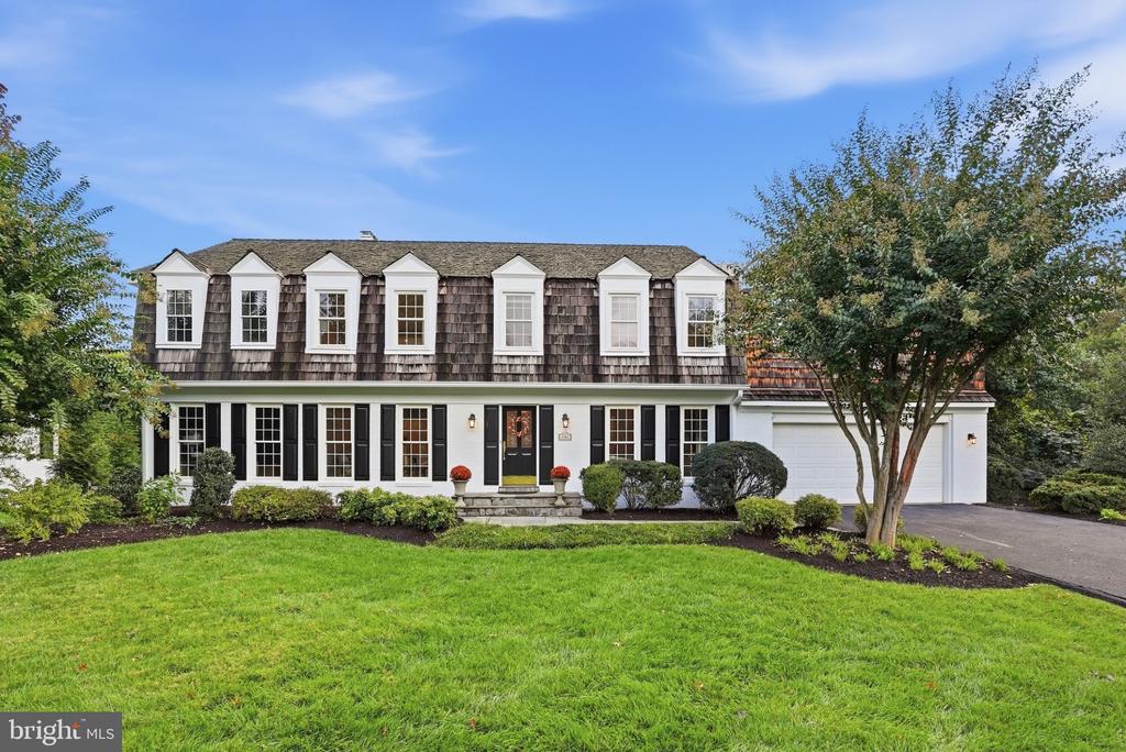 Two-story house with a row of dormer windows, attached garage, and landscaped front lawn.