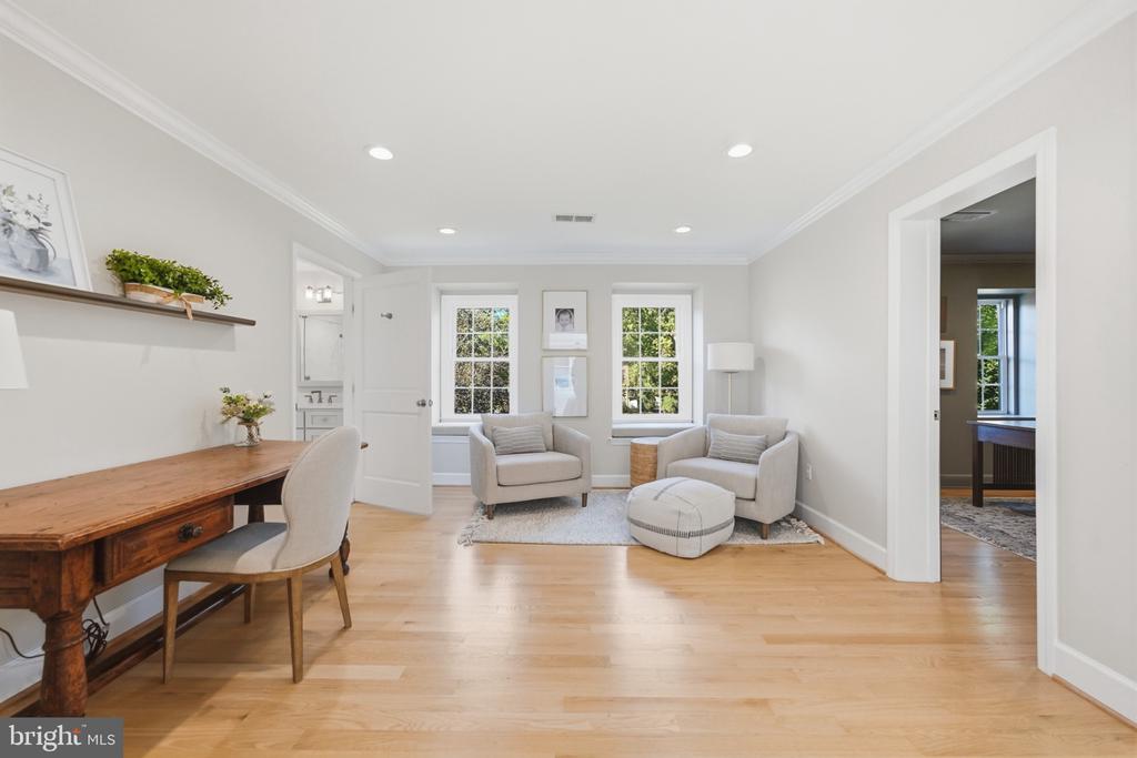 Bright sitting room with two armchairs and ottoman, a wooden desk, and hardwood floors.