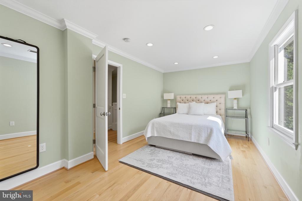 Bedroom with a tufted bed, pale green walls, hardwood floors, and a large window.