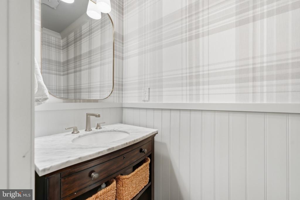 Bathroom vanity with a marble countertop, dark wood cabinet, plaid wallpaper, and white beadboard walls.