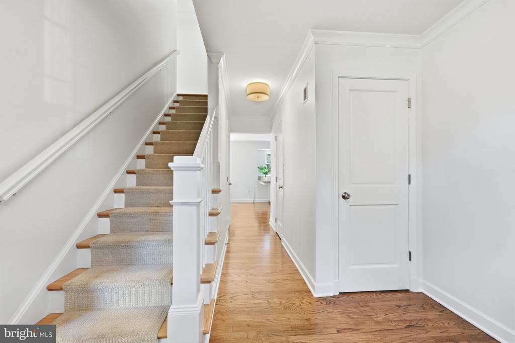 Hallway with a carpeted staircase, wood flooring, and a closed white door.