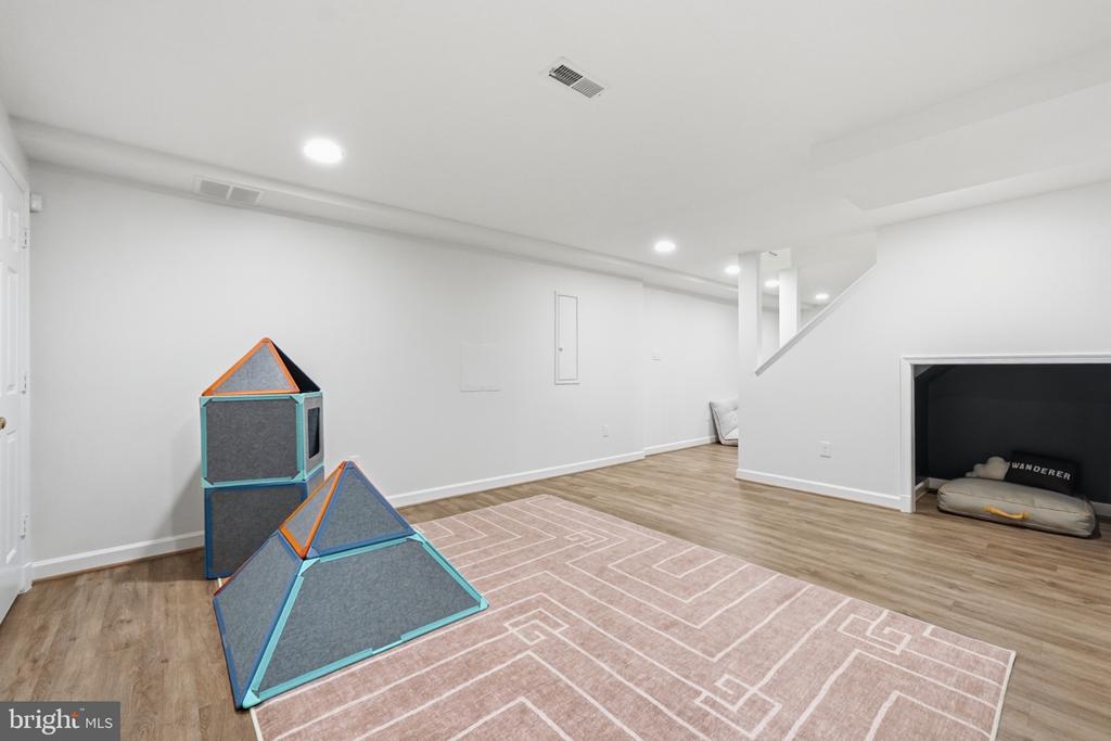Finished basement recreation room with a patterned rug, children's climbing structures, and a pet nook beneath the stairs.