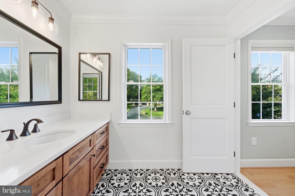 Bathroom with a wood vanity, large mirror, two windows, and patterned black-and-white tile floor.