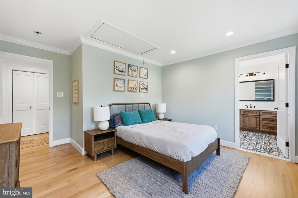 Furnished bedroom with a wooden bed, teal pillows, hardwood floors, and an adjoining bathroom.