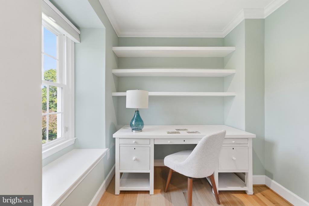 Home office with a white desk, built-in shelves, and a window seat.