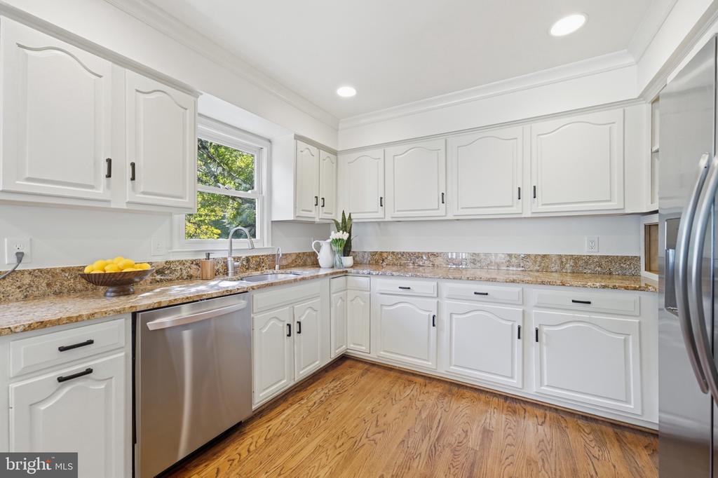 Kitchen with white cabinets, granite counters, stainless steel appliances, and hardwood floors.