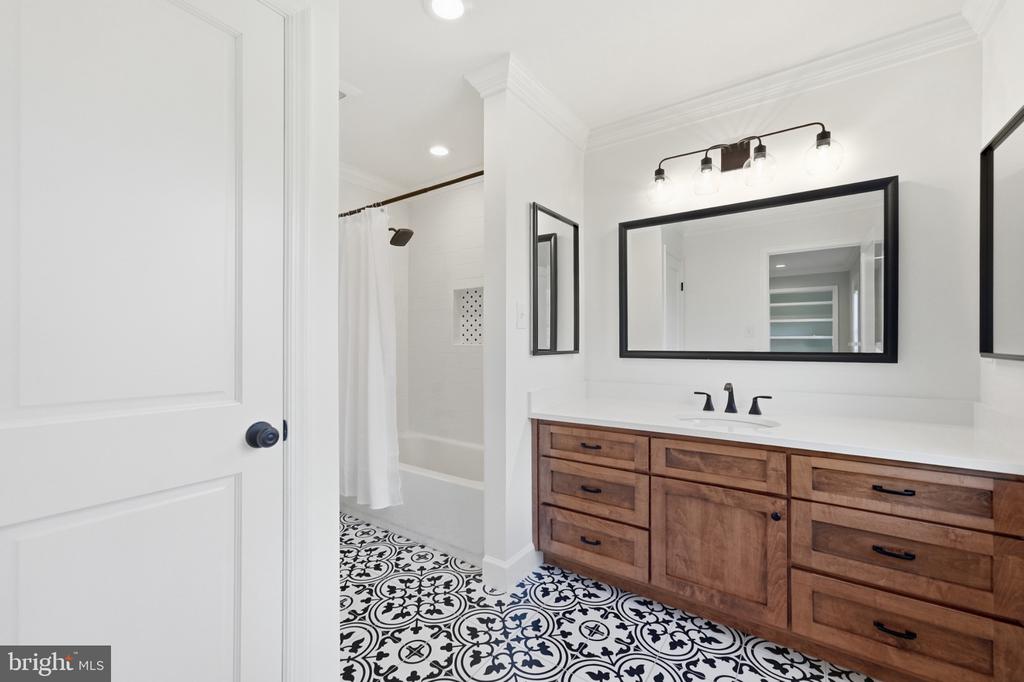 Bathroom with a wood vanity, black-framed mirror, and patterned tile floor.