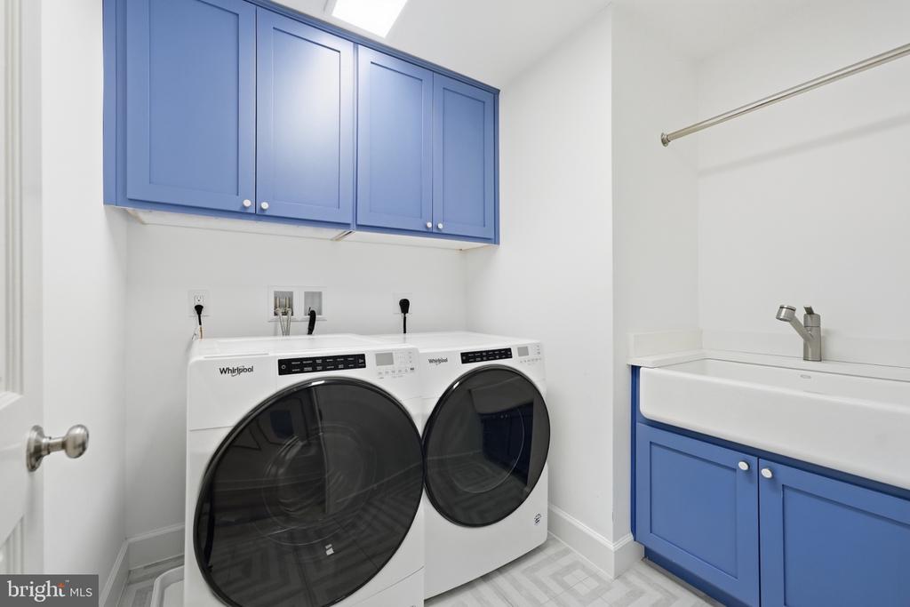 Laundry room with two front-loading machines, blue cabinets, and a utility sink.